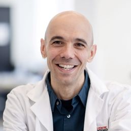 A bald man in a white lab coat smiles at the camera