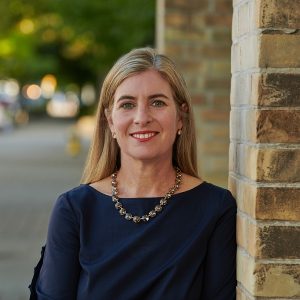 Professor Melanie Woodin standing on a treed path next to a brick wall