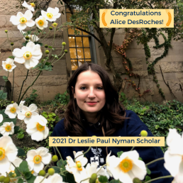 Alice DesRoches, 2021 Nyman Scholar sits in a stone courtyard with trees and flowers around her