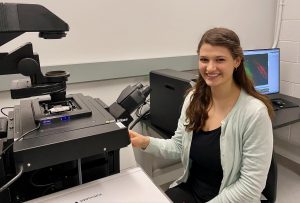 Natalie Hoffmann sits at a large microscope stage.